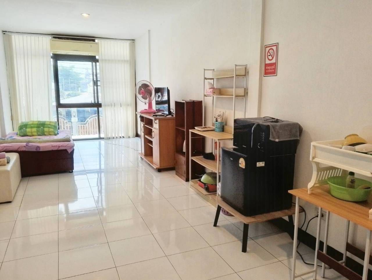 A clean, well-lit room with a sofa, a fan, a TV, and a refrigerator.