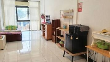 A clean, well-lit room with a sofa, a fan, a TV, and a refrigerator.