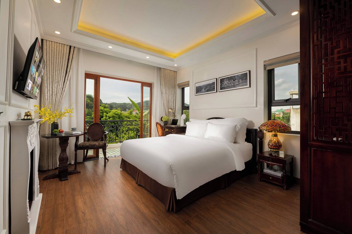 Une chambre d’hôtel avec un grand lit, un bureau avec une chaise, un téléviseur fixé au mur et une fenêtre donnant sur un paysage verdoyant.