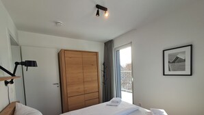 A bedroom with a wooden wardrobe, a bed with white linens, a bedside lamp, and a framed picture on the wall. - Modern vacation apartment with exceptional views and its own infrared cabin (Winterberg)