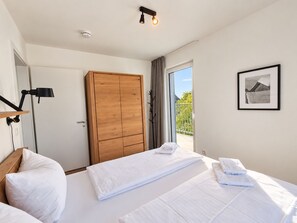 A hotel room with two beds, a wooden wardrobe, a desk with a lamp, a framed picture on the wall, and a balcony with a view. - Modern vacation apartment with exceptional views and its own infrared cabin (Winterberg)