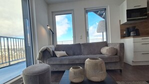 A modern living room with a grey sofa, two windows, a coffee machine, and a view of the city. - Modern vacation apartment with exceptional views and its own infrared cabin (Winterberg)