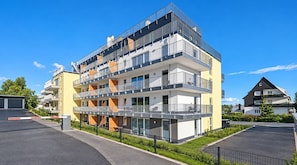 A multi-story residential building with balconies, a gated driveway, and a clear sky.