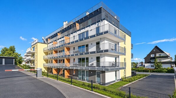 A multi-story residential building with balconies, a gated driveway, and a clear sky.