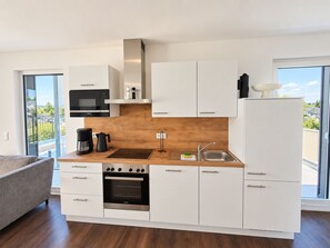A modern kitchen with white cabinets, a built-in oven, a coffee maker, and a view of the outdoors. - Modern vacation apartment with exceptional views and its own infrared cabin (Winterberg)