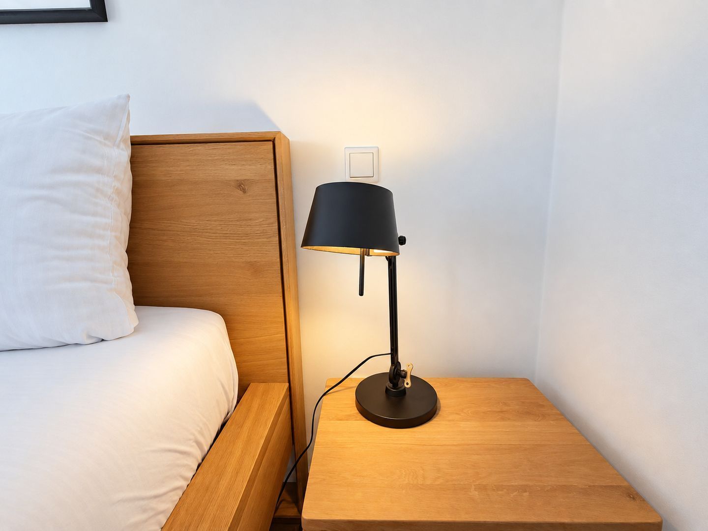 Ein Bett mit Holz Kopfteil, ein Nachttisch mit Lampe und ein an der Wand befestigter Lichtschalter.