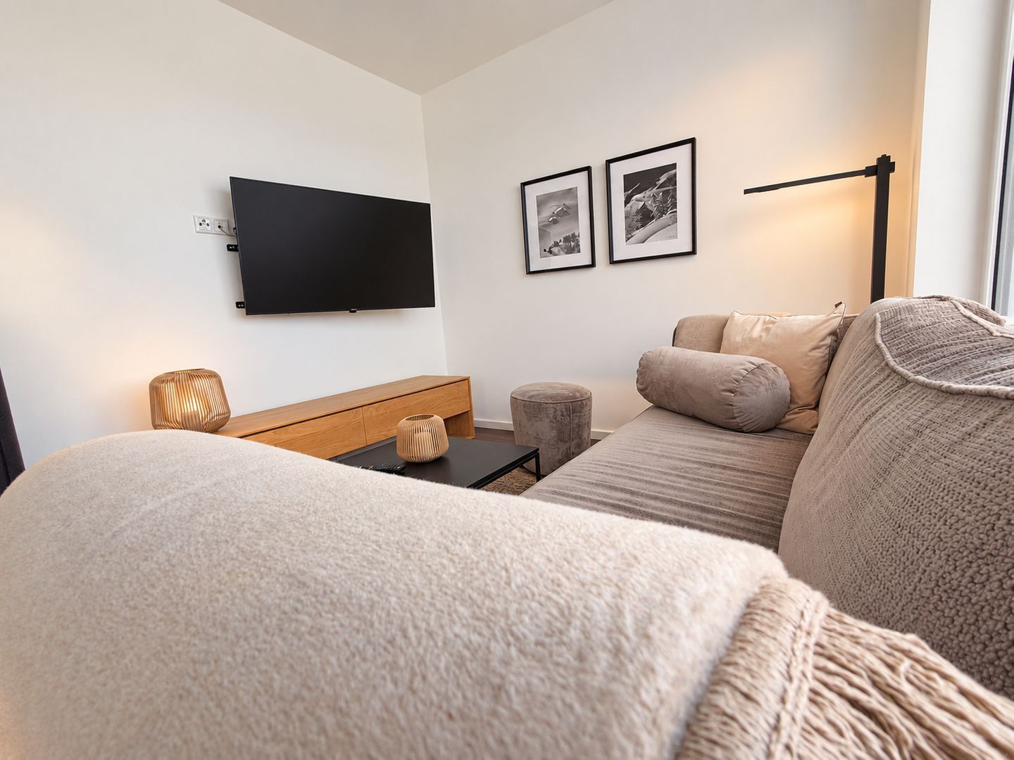 A modern living room with a flat-screen TV, a sofa, a coffee table, and a lamp.
