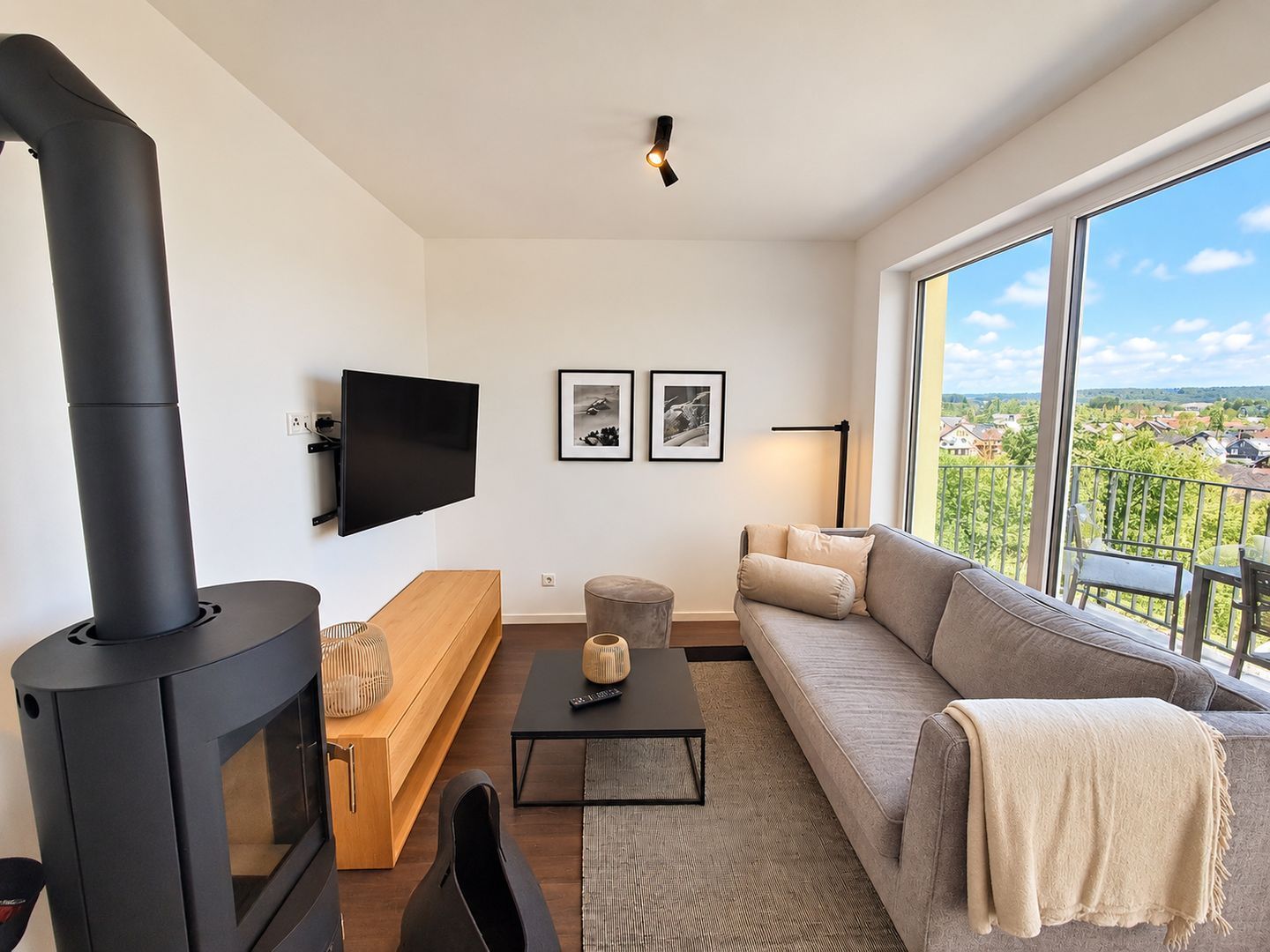 A modern living room with a large black fireplace, a flat-screen TV, a sofa, and a view of a green landscape through large windows.