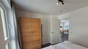 Quarto de hotel com guarda-roupa de madeira, cama com roupa de cama branca, mesa de cabeceira e vista para a sala de jantar.