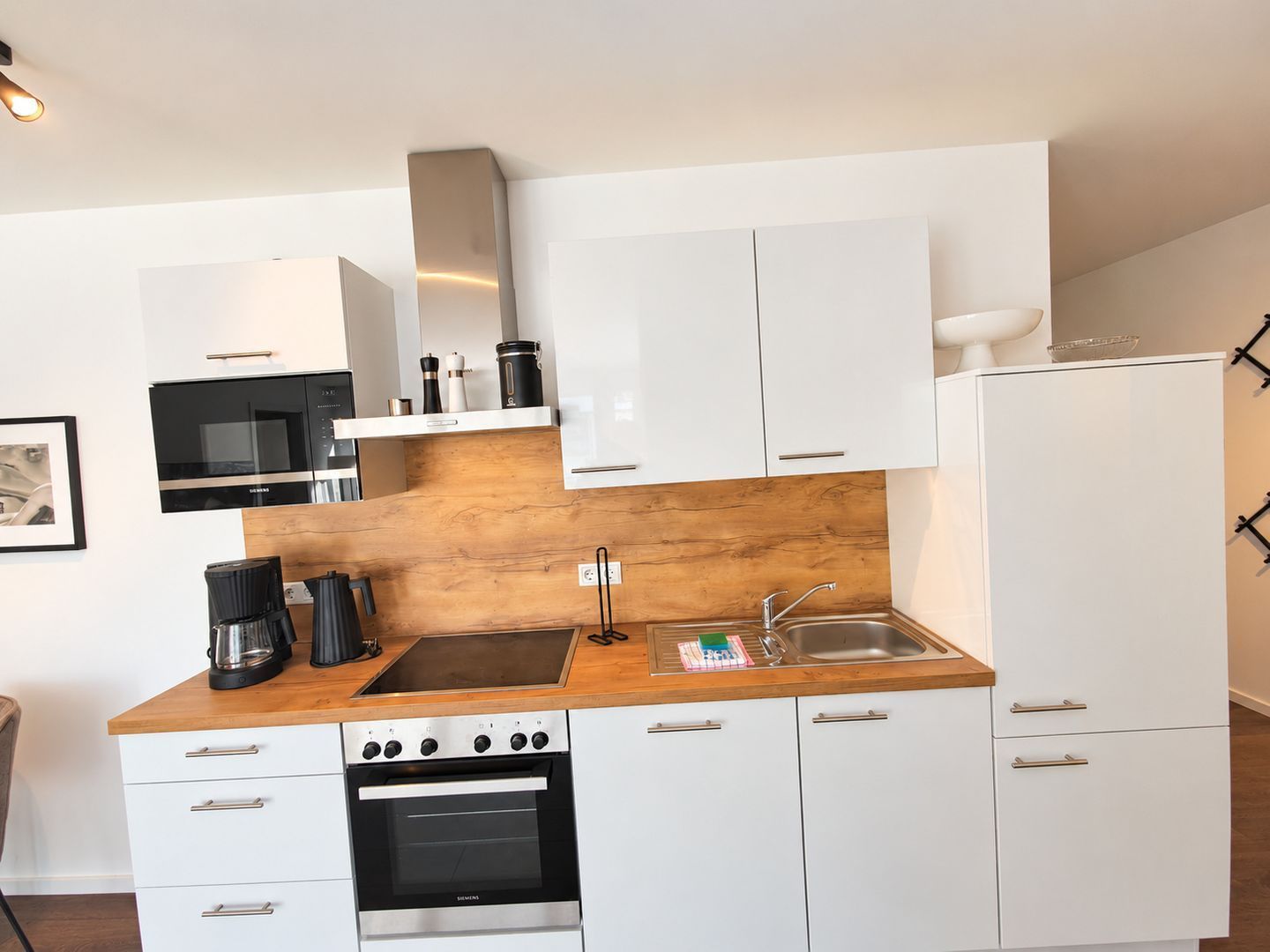 A modern kitchen with white cabinets, a stainless steel oven, a coffee maker, and a microwave.