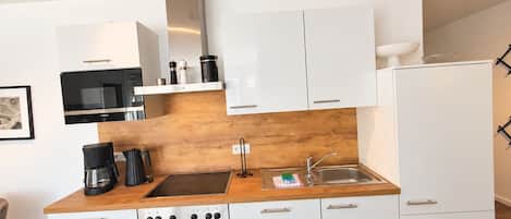 A modern kitchen with white cabinets, a stainless steel oven, a coffee maker, and a microwave.