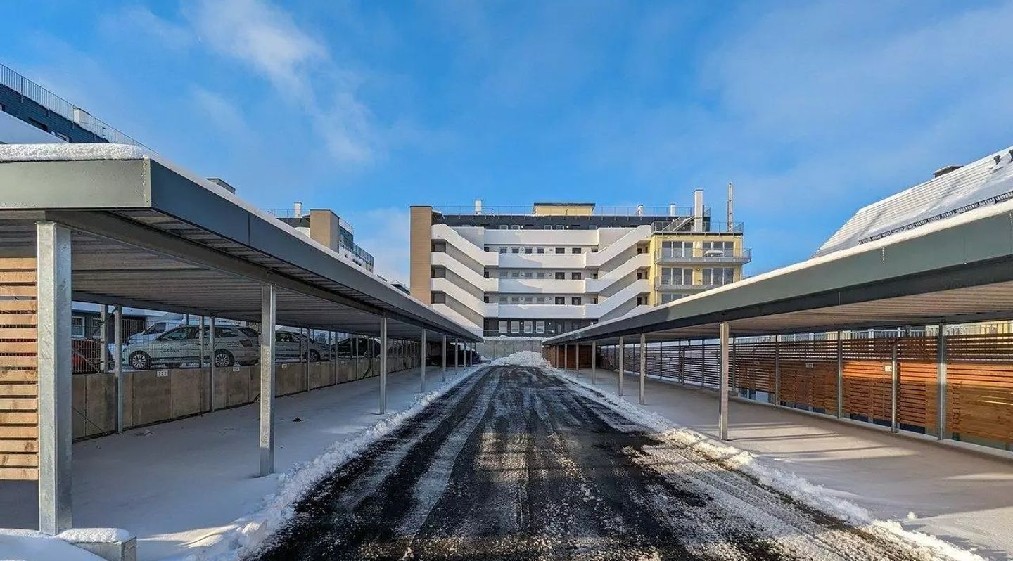 A covered parking area with a central pathway leading to a building with multiple floors and a flat roof.