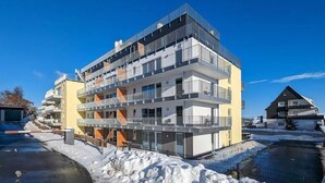 Un edificio de varios pisos con balcones, una entrada con portón y nieve en el suelo.