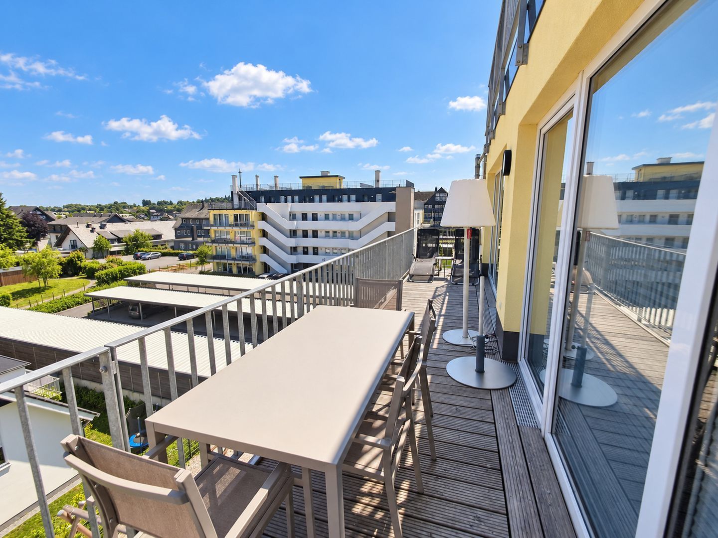 Een balkon met een tafel en stoelen, met uitzicht op een woonwijk met huizen en een heldere lucht.