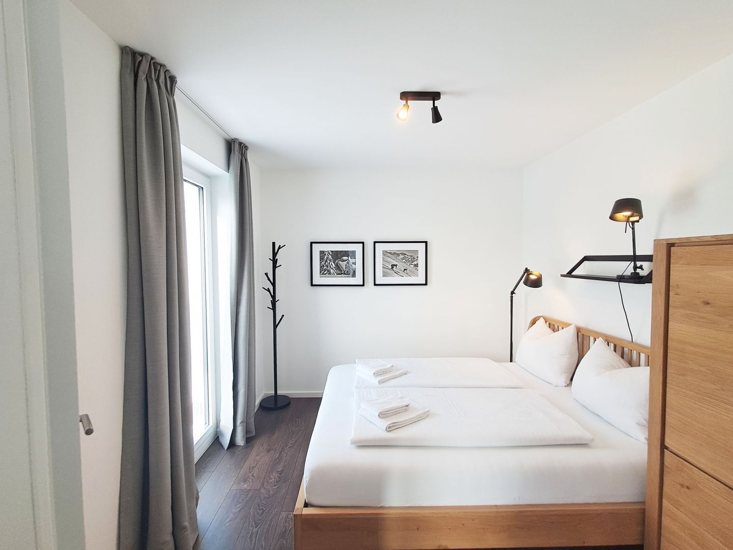 Een moderne hotelkamer met een groot bed, een nachtkastje met lamp en twee ingelijste foto’s aan de muur.
