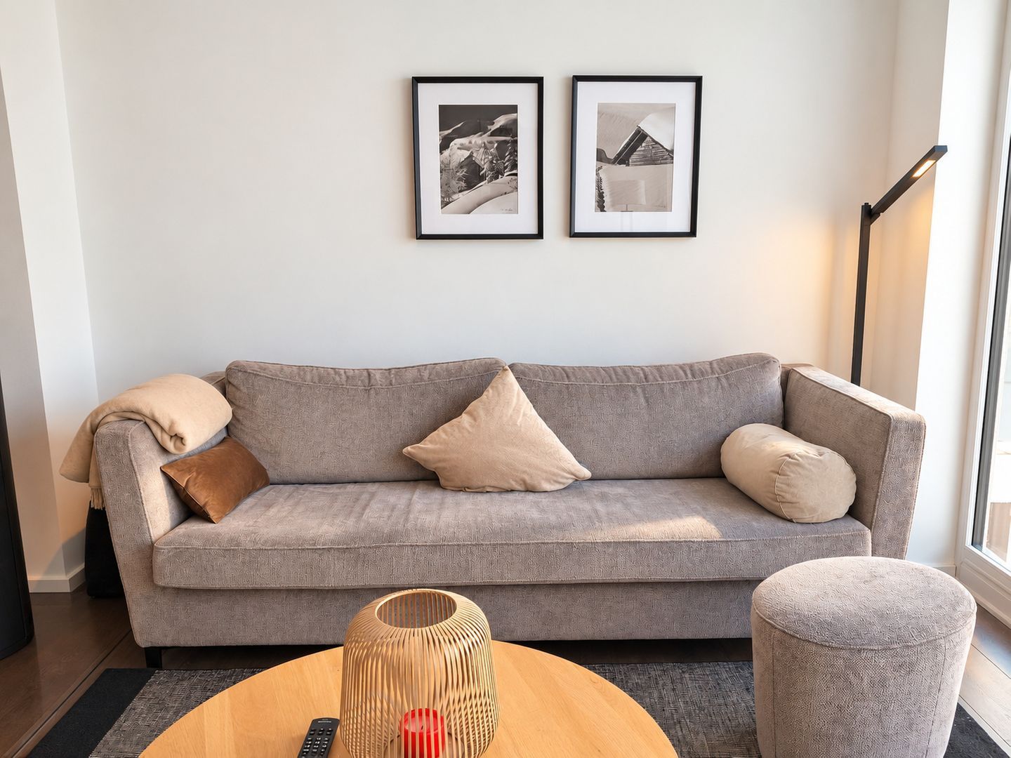 A living room with a grey sofa, a round wooden coffee table, a floor lamp, and two framed pictures on the wall.