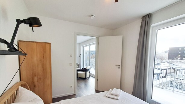 Habitación de hotel con cama, escritorio, silla, lámpara y vistas al exterior.