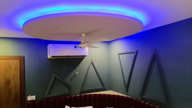 Een kamer met een plafondventilator, een airconditioning en decoratieve driehoekige wandpanelen.