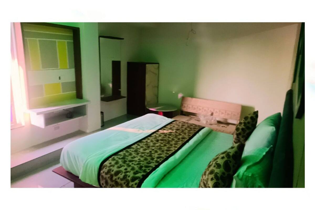 A bedroom with a bed, a mirror, a small table, and a window.