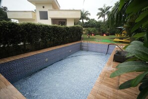 A swimming pool with a tiled edge, surrounded by a wooden deck and a hedge.