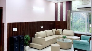 A living room with a sectional sofa, a round coffee table, and a teal armchair. - Mango People Farm (Sohna)