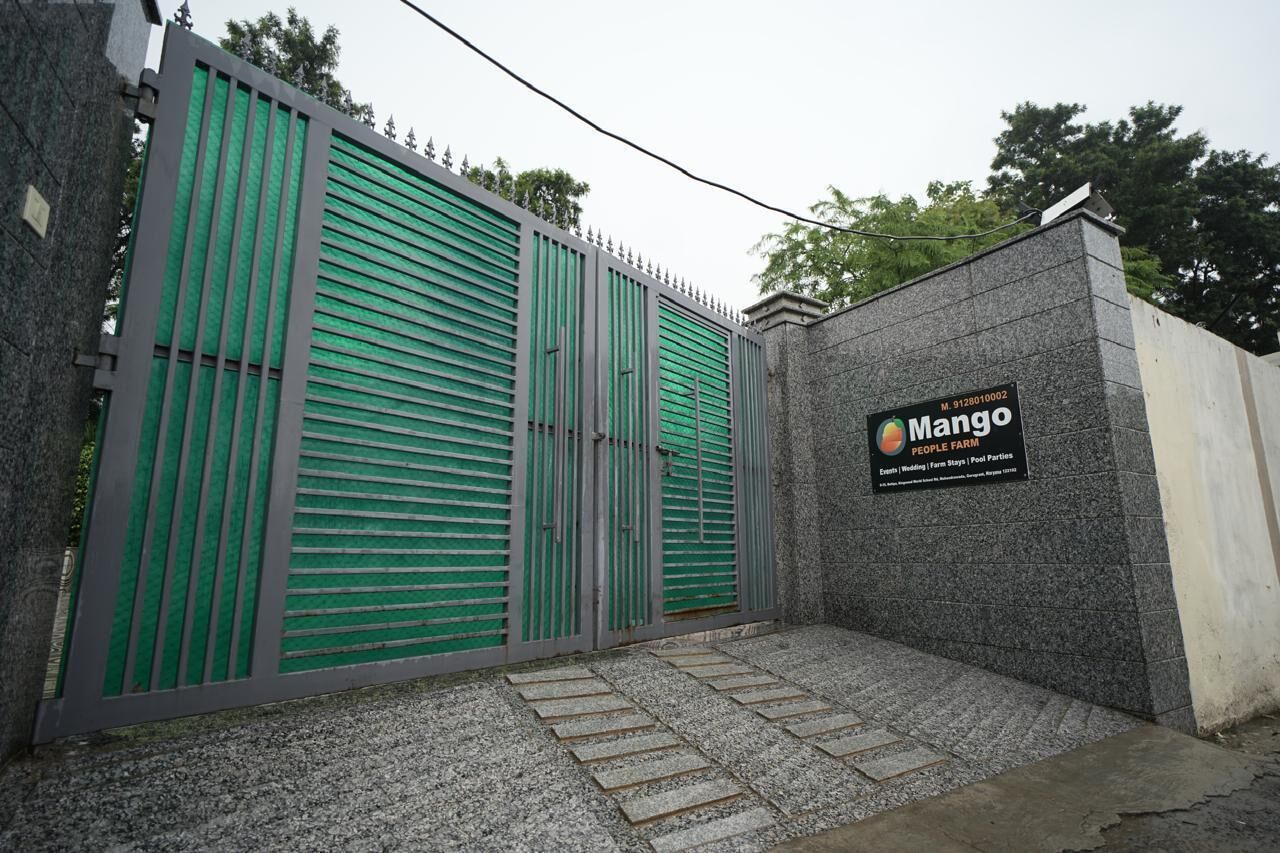 Una entrada cerrada con un letrero de Mango People Farm, que presenta un muro de piedra y una reja metálica con listones verdes.