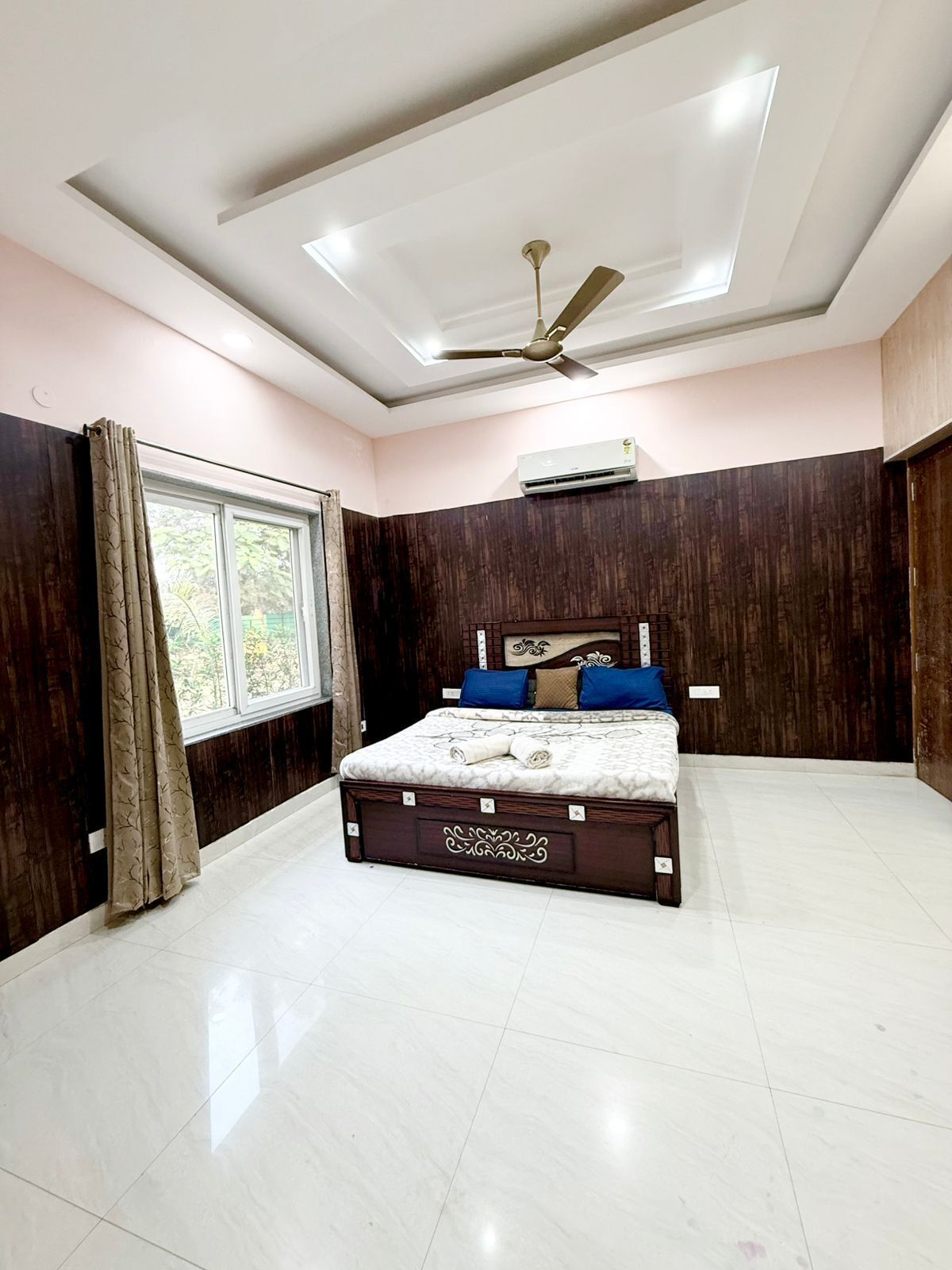 Un dormitorio con cama, ventilador de techo, unidad de aire acondicionado y ventana con cortinas.