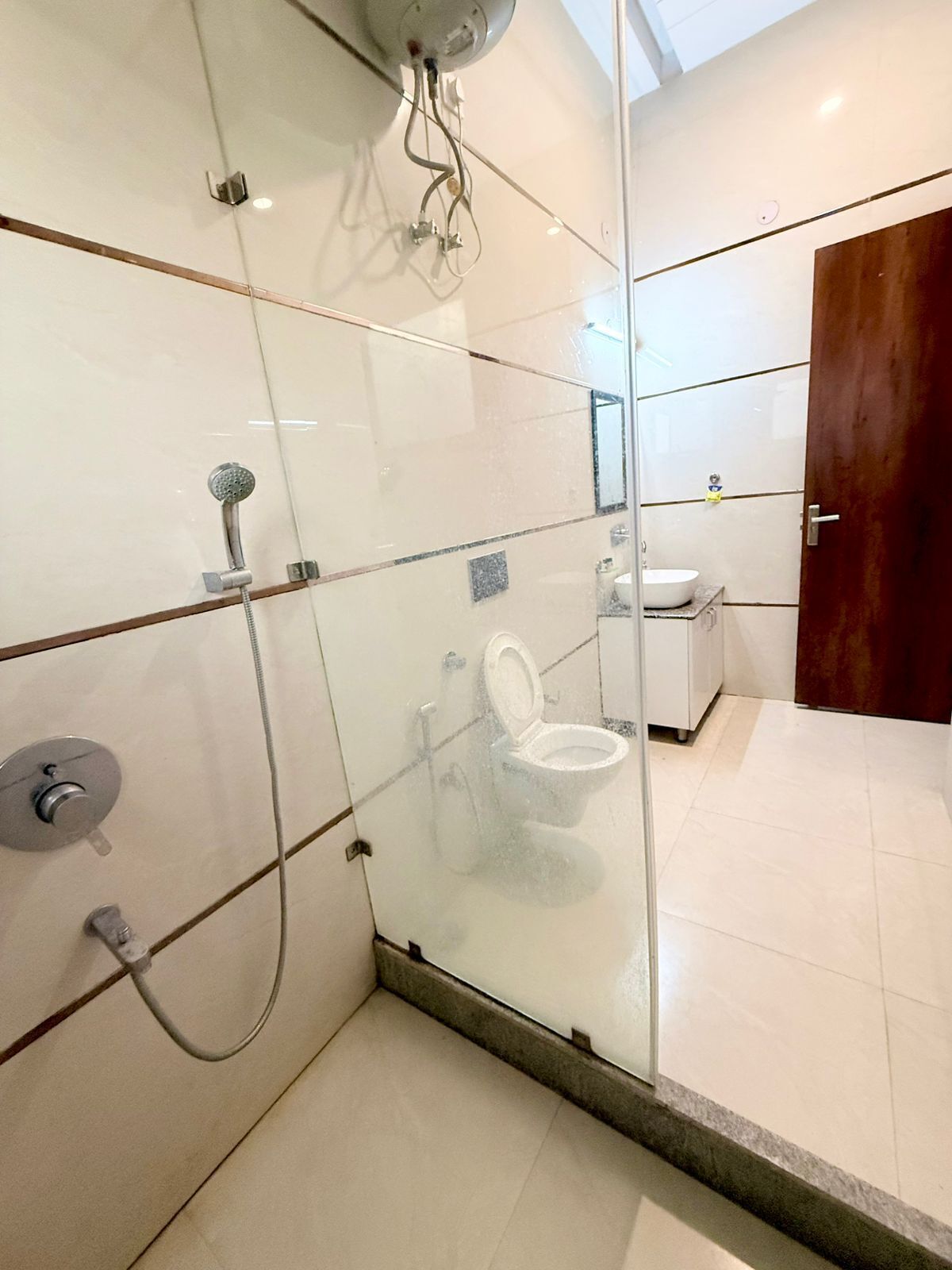 A modern bathroom with a glass-enclosed shower, a toilet, and a sink.