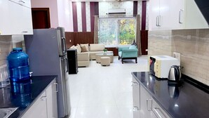 A modern kitchen with stainless steel appliances, a water dispenser, and a dining area with a sofa and coffee table. - Mango People Farm (Sohna)