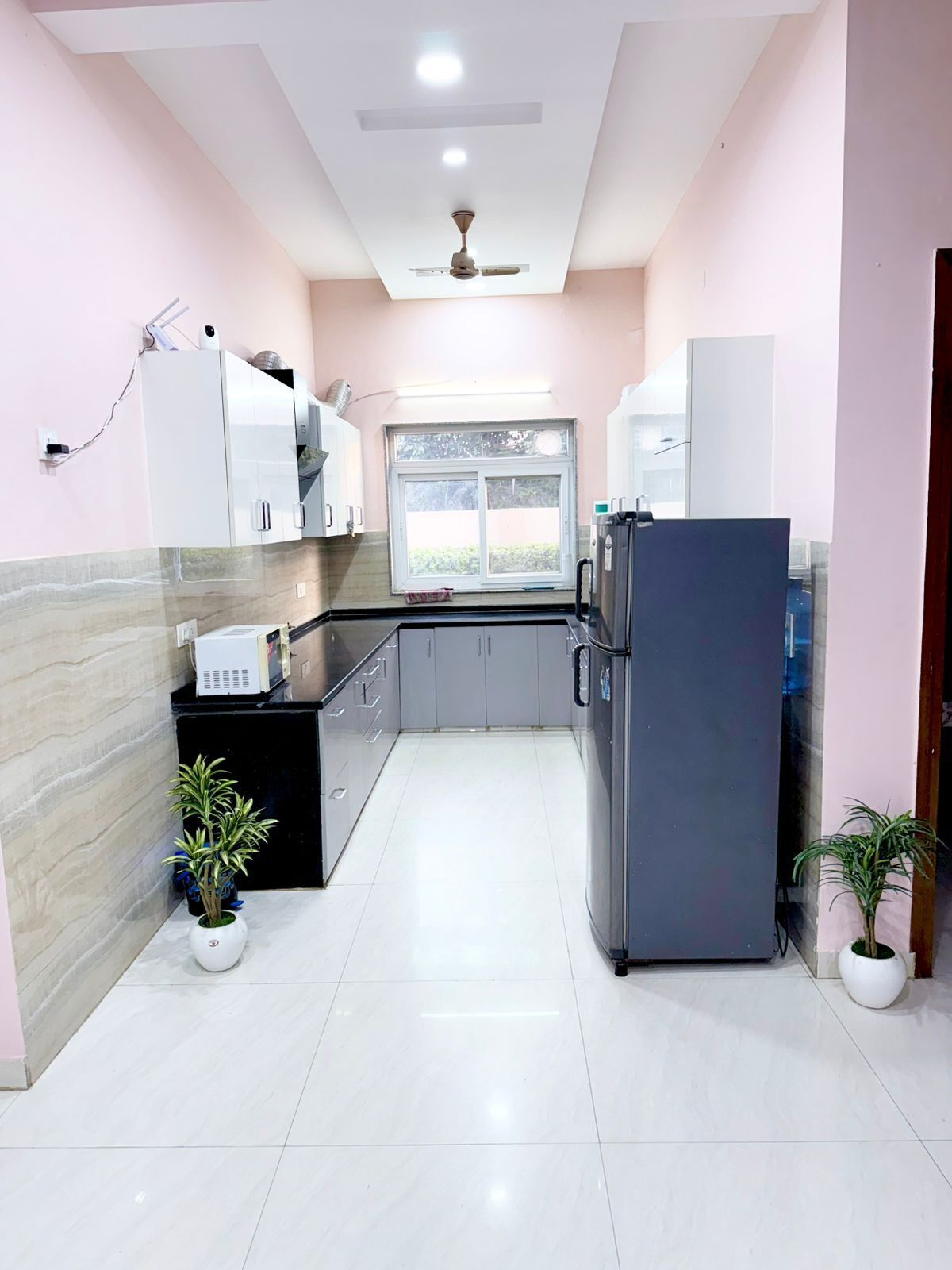A modern kitchen with white cabinets, a black countertop, and a built-in refrigerator. There is a window providing natural light and a ceiling fan.