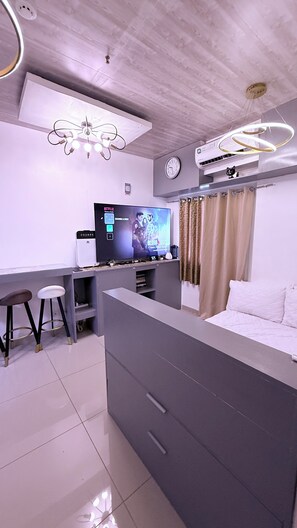 A modern room with a bed, a desk, a TV, and a ceiling fan.