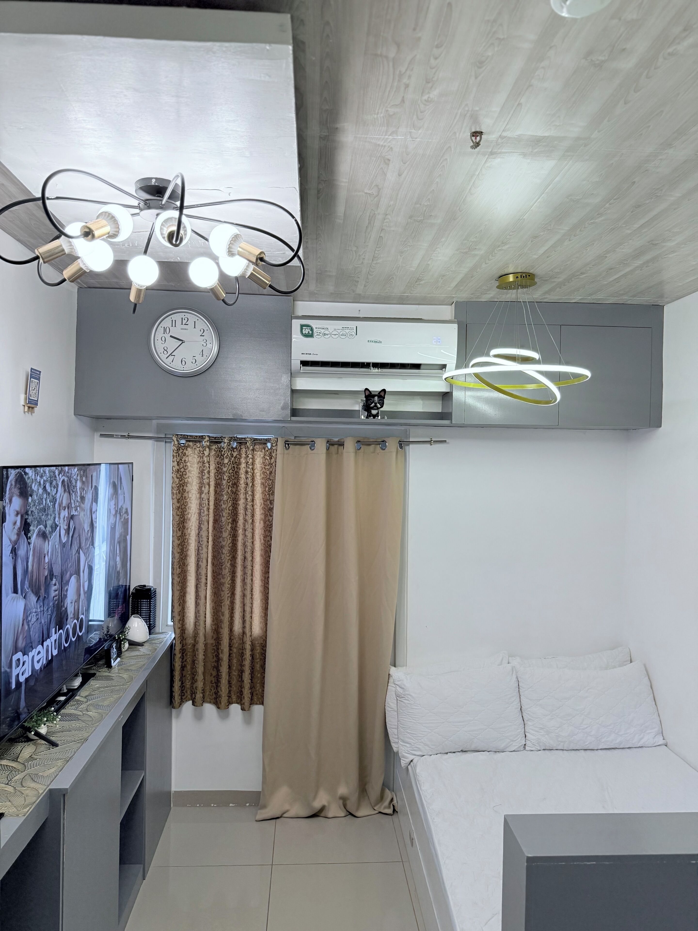 A modern living room with a flat-screen TV, a ceiling fan, an air conditioner, and a bed.