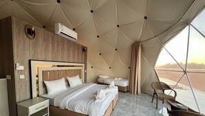 Ein schlafraum im Zeltstil mit einem großen Bett, einem Nachttisch, einem Sessel und Blick auf die Wüste durch ein großes Fenster.