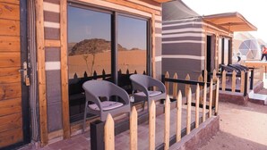 A wooden building with large windows, a wooden fence, and two chairs outside. - Shaheen Camp Wadi Rum – Deluxe Tent (العقبه)