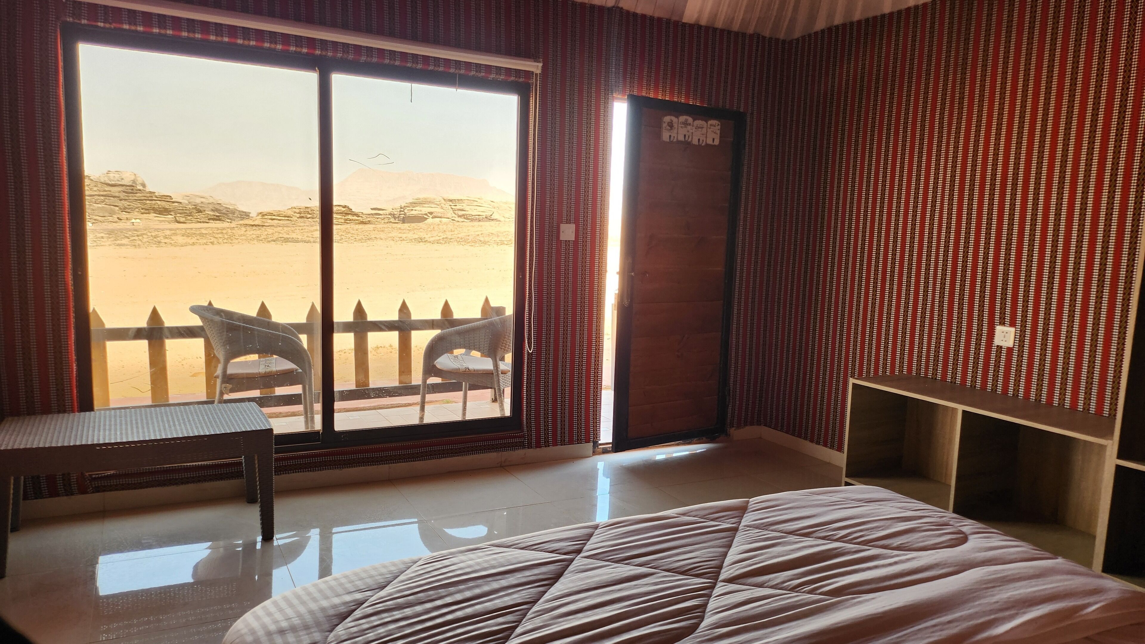 A room with a bed, a table, and chairs near a large window with a view of a desert landscape.