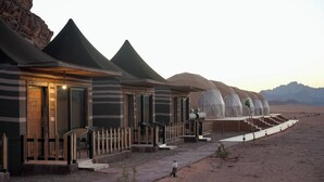 A desert resort with multiple dome-shaped tents, each with a small porch and seating area. - Shaheen Camp Wadi Rum – Deluxe Tent (العقبه)