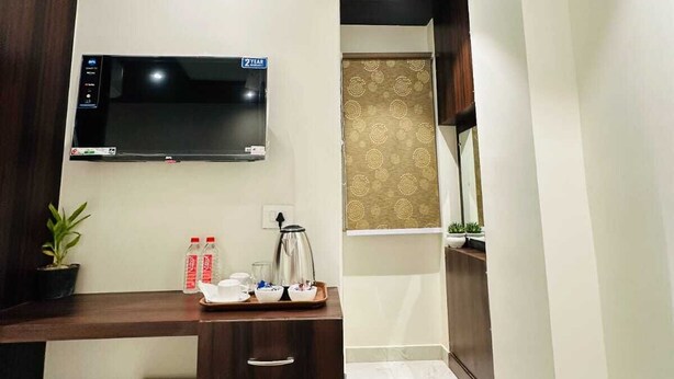 A compact hotel room with a kitchenette, a flat-screen TV, a small desk with a coffee maker, and a potted plant. - Kashi Darshan Hotel (Varanasi)