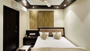 A modern bedroom with a large bed, a ceiling fan, and a nightstand with a lamp. - Kashi Darshan Hotel (Varanasi)