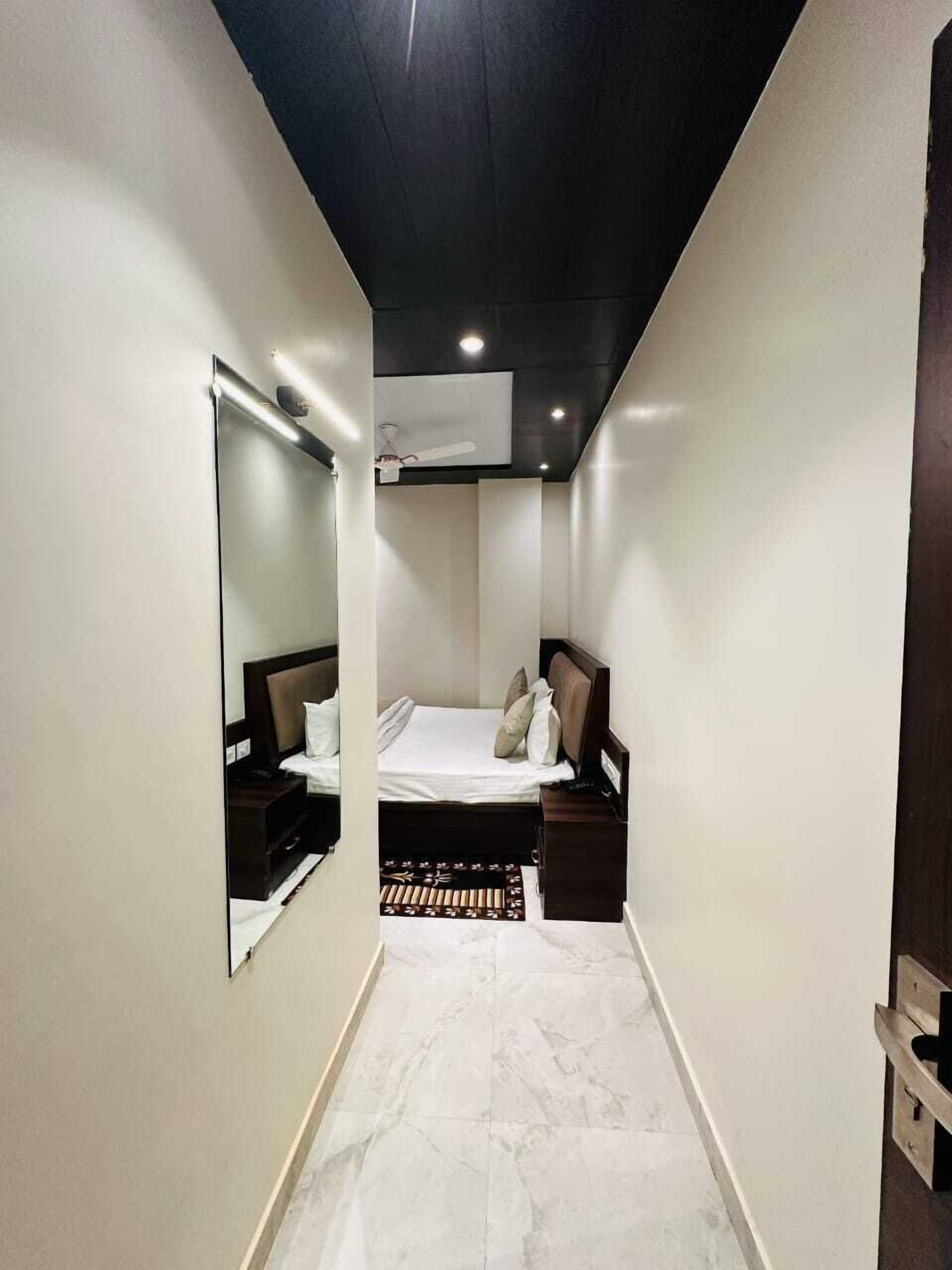 A narrow hotel room with a bed, bedside tables, a mirror, and a ceiling-mounted air conditioner.