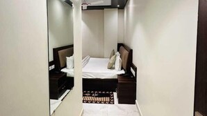 A narrow hotel room with a bed, bedside tables, a mirror, and a ceiling-mounted air conditioner. - Kashi Darshan Hotel (Varanasi)