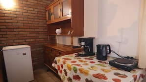 Cocina compacta con refrigerador, cafetera y mesa con mantel estampado de frutas.