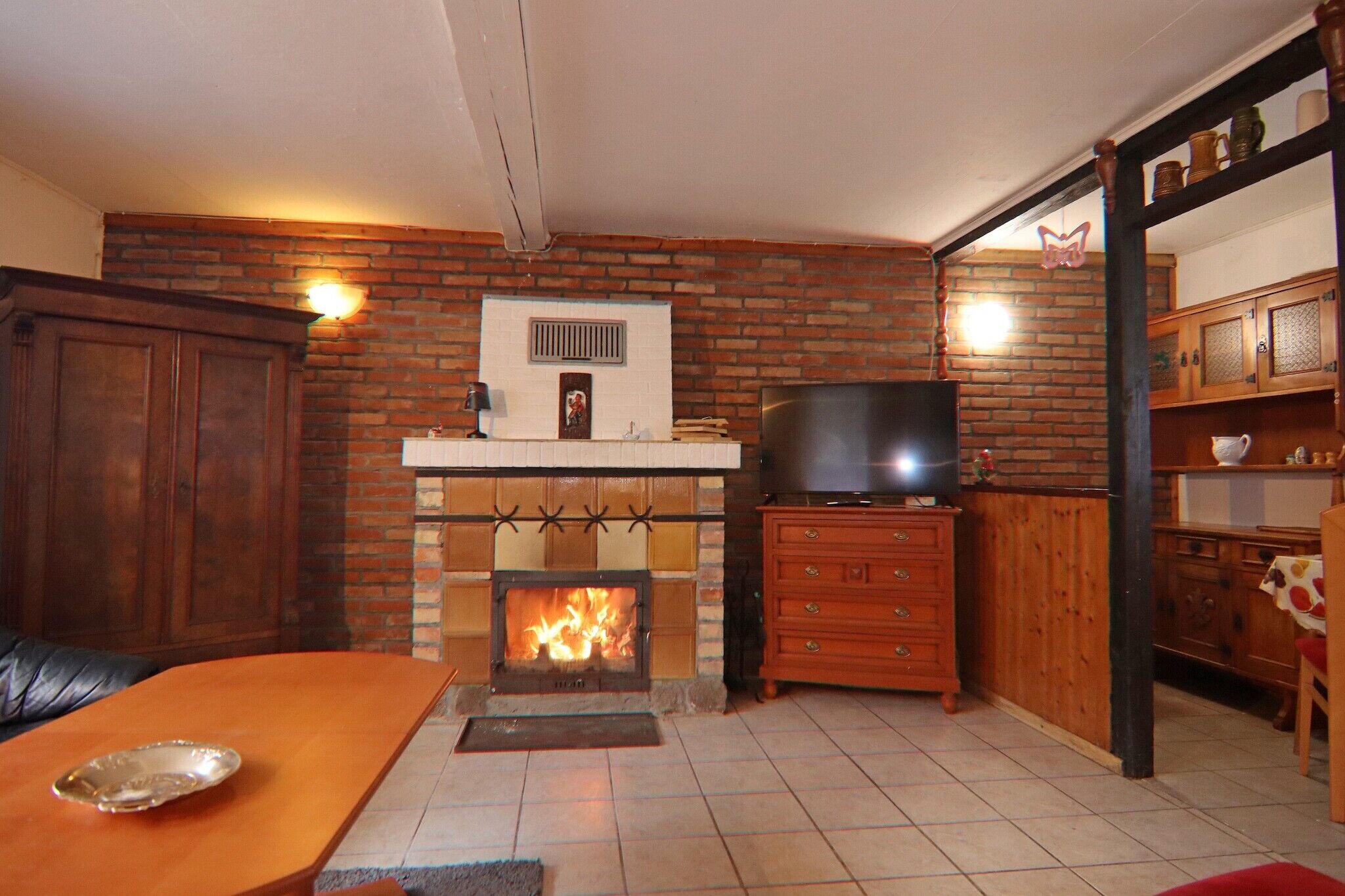 A living room with a brick fireplace, wooden furniture, and a television.