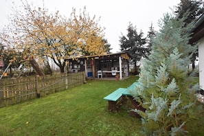 A wooden cabin with a porch, a picnic table, and a fenced yard with a tree.