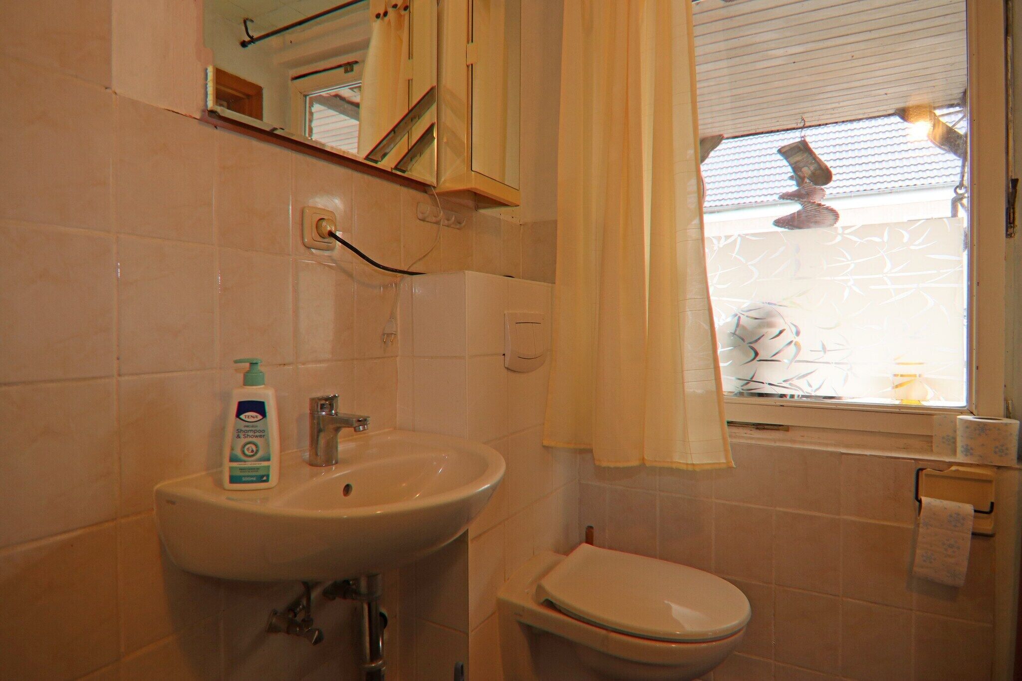 Une salle de bain avec un lavabo, des toilettes et une fenêtre avec un rideau.