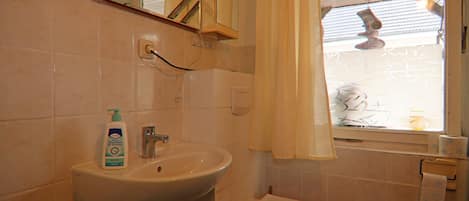 Une salle de bain avec un lavabo, des toilettes et une fenêtre avec un rideau.