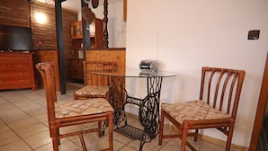 Un comedor con dos sillas de madera, una mesa de vidrio, un aparador de madera y un televisor sobre un tocador.