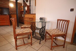 A dining area with two wooden chairs and a glass table, a wooden cabinet, and a television on a dresser.