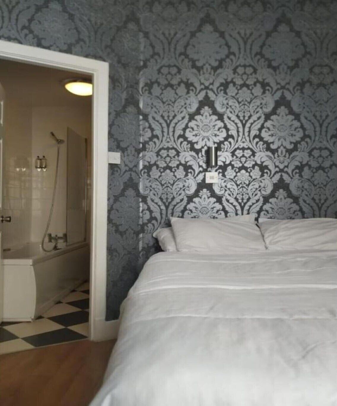 Un dormitorio con cama, un baño con ducha y un papel tapiz estampado.