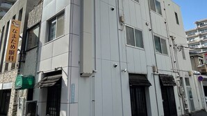 A modern building with a flat facade, multiple windows, and a visible entrance with a door. - Convenient Nakano Home near Station - Perfect for Budget Travelers (31) (中野区中央)