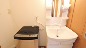 A compact bathroom with a white sink, a mirror, and a black and white heater. - Convenient Nakano Home near Station - Perfect for Budget Travelers (31) (中野区中央)